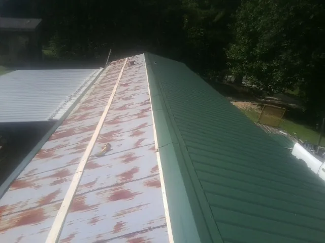 Old rusted panels beside newly installed green metal roofing — Wind Damage Roof Repair by Roofing Brothers in Vernon