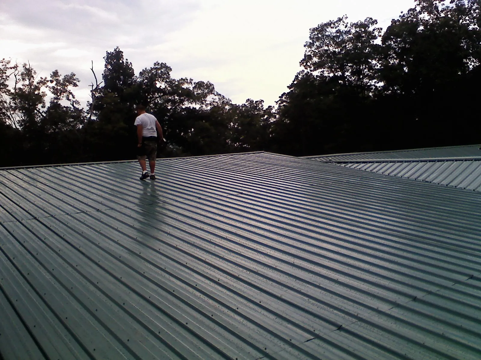 Roofer walking a wide expanse of new green metal roofing in Vernon