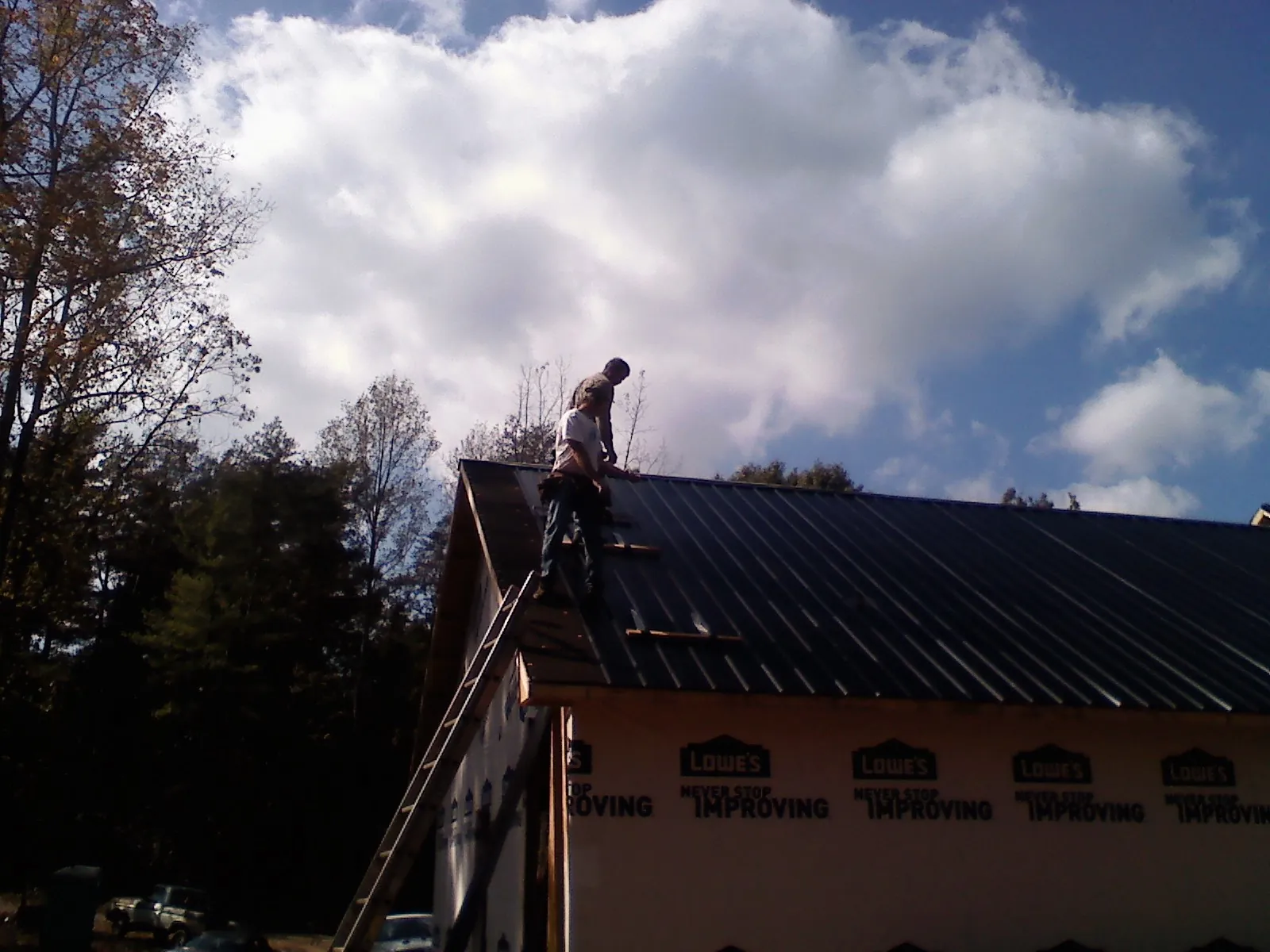 Roofer fastening dark metal panels high against a cloudy sky, from a Roof Inspection job in Vernon